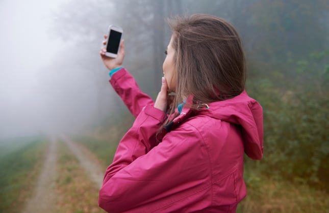 women looking at phone in misty woods