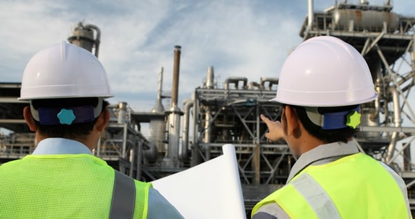 Two men holding a blueprint plan, pointing at a factory