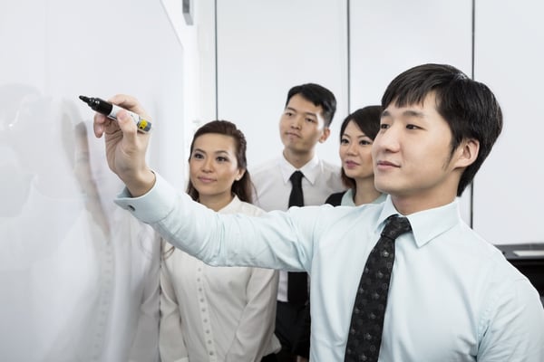 Colleagues surrounding a white board figuring out a problem