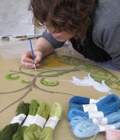 Artist painting a needlepoint rug pattern on a canvas