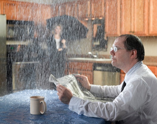 man drinking coffee in kitchen while it rains inside due to leaky roof