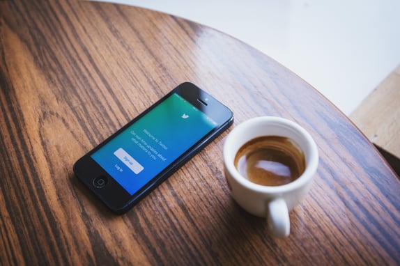 A phone on a table next to a mug of coffee to represent B2B social media