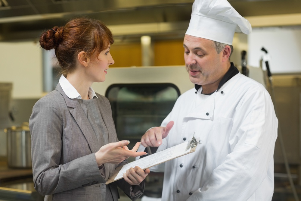 Young female manager talking to the head cook standing in a professional kitchen