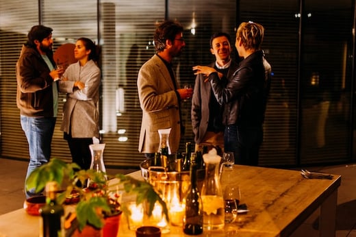 Groups of people chatting during a happy hour in front of a table of beverages and candlelight 