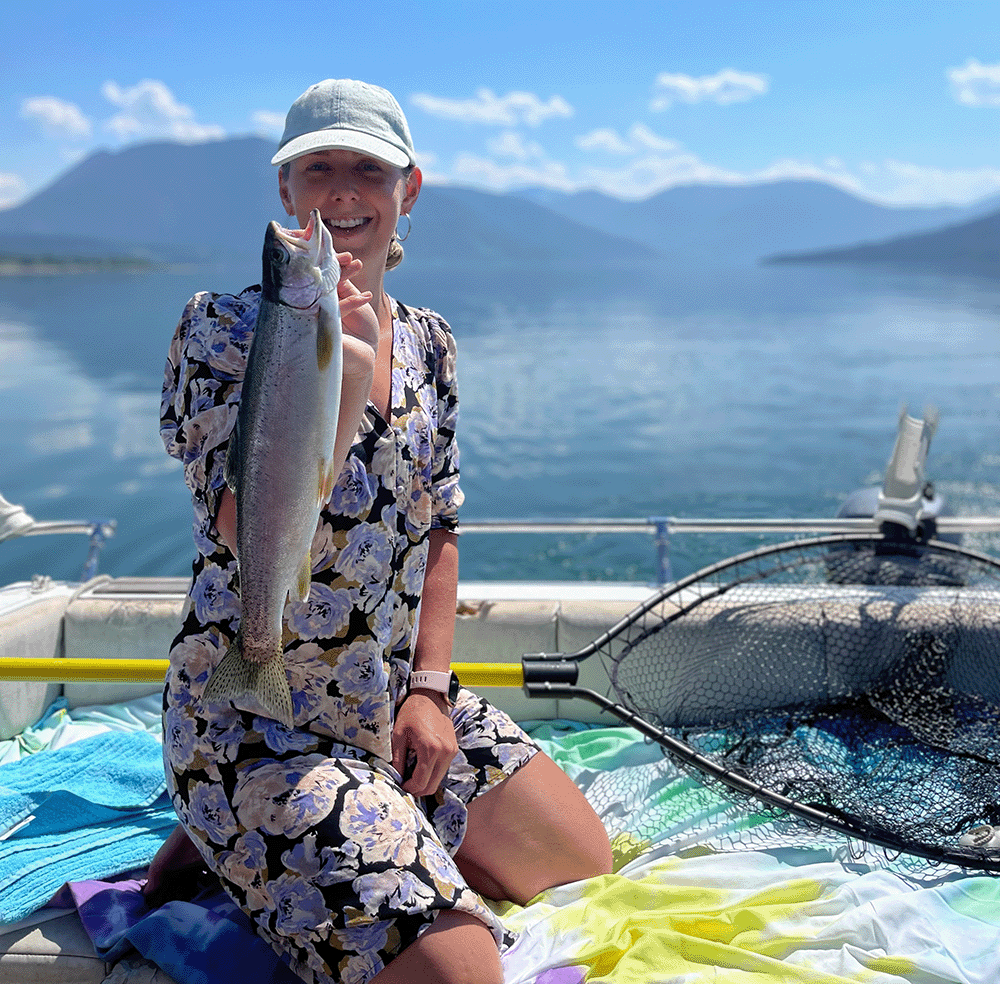 Rory holding a fish in the back of boat with lake in background.