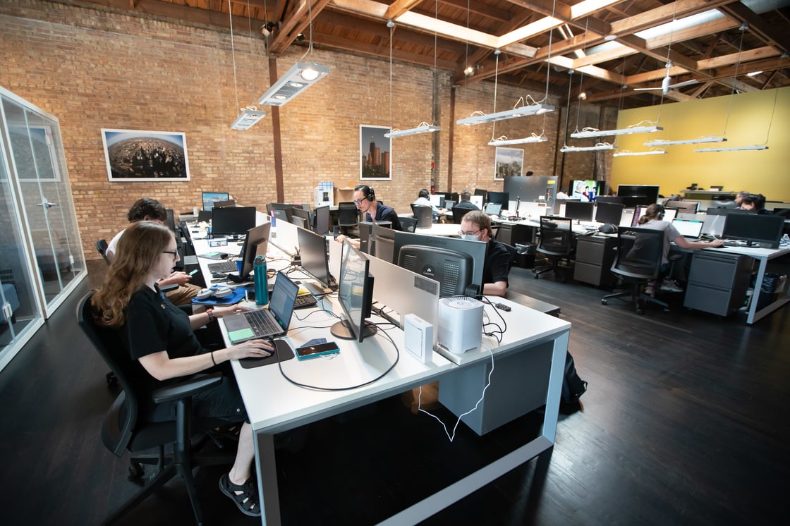 Aspiritech office workers in modern office with exposed brick wall and loft ceiling with wooden beams.