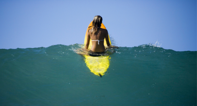 Rear view of a young woman sitting on a surfboard