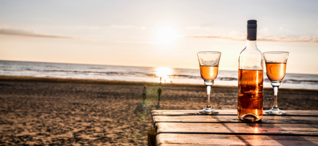 a bottle of rose' and two glasses on beach with sunset