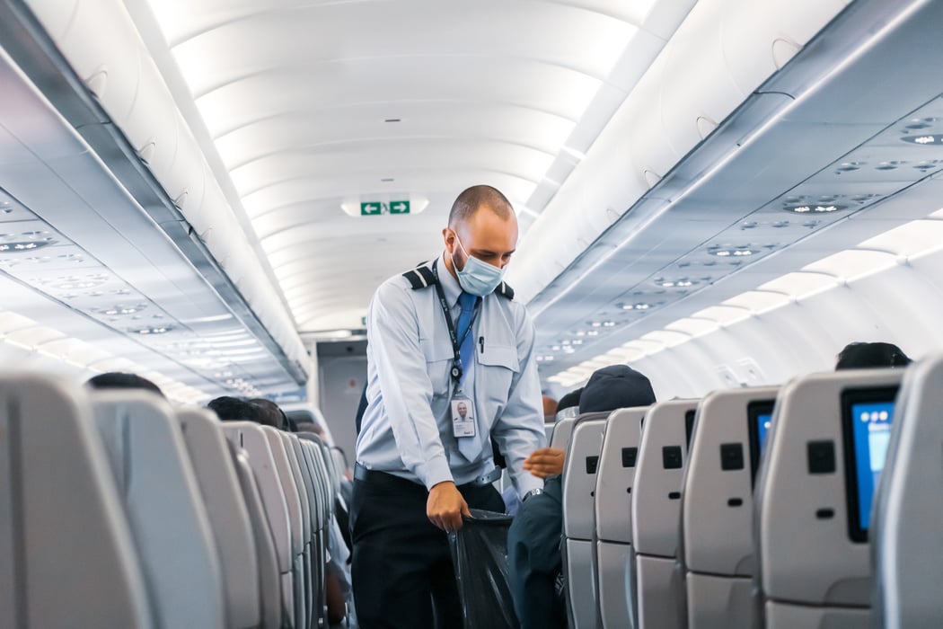 An air steward walks down the aisle of an airplane with a garbage bag. 