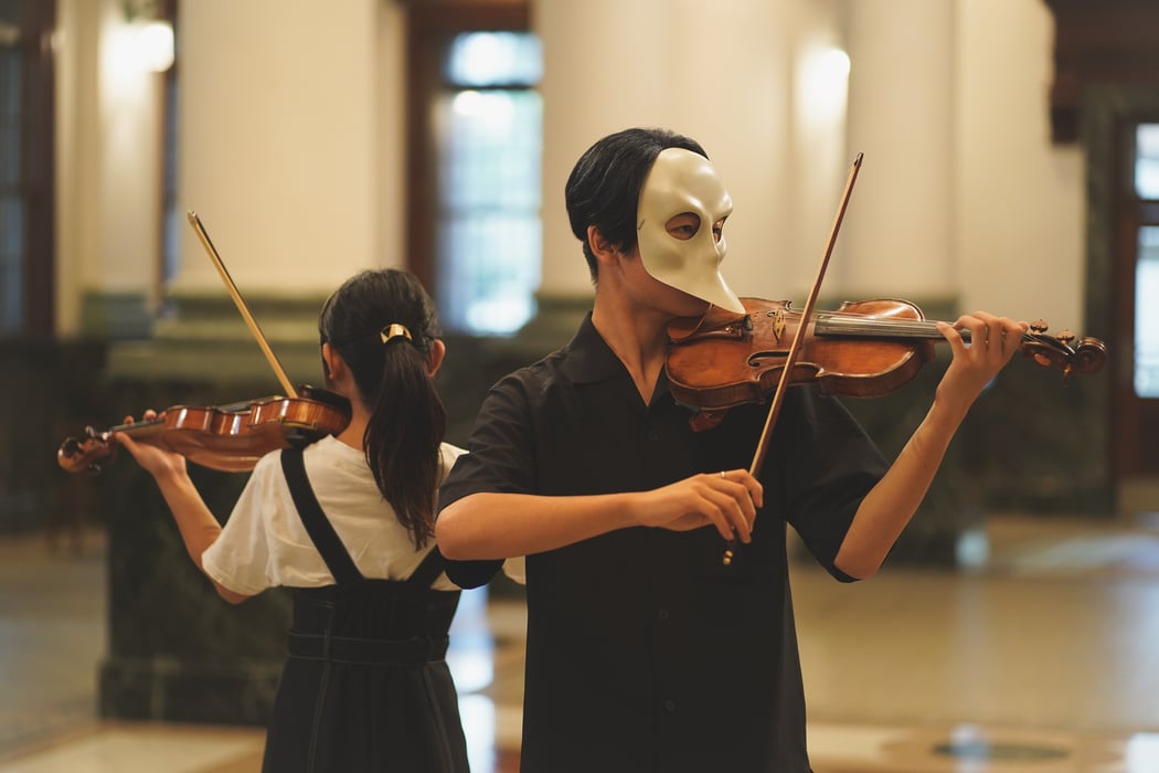 A masked duo plays the violin.