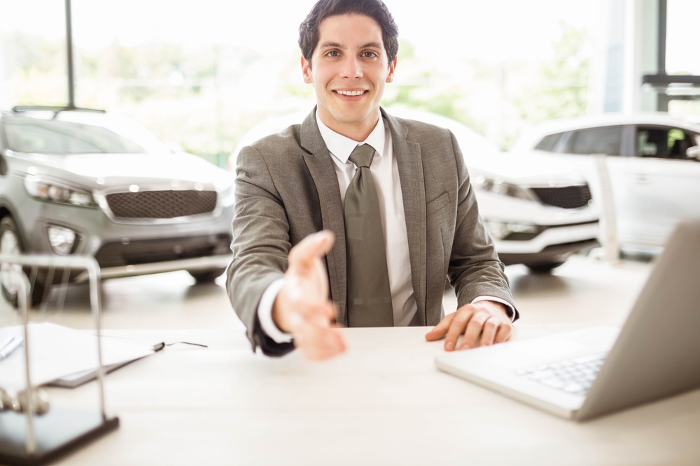 Smiling salesman ready to shake hand at new car showroom
