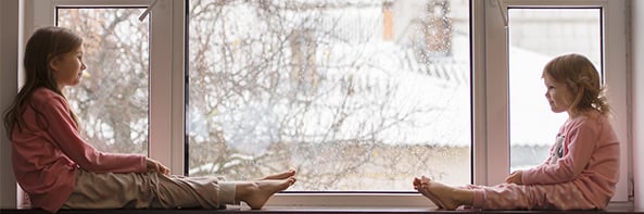 Two young girls sitting on a windowsill on a rainy day