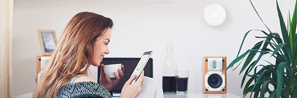 Woman relaxing with a coffee while checking the Airthings app on her mobile phone