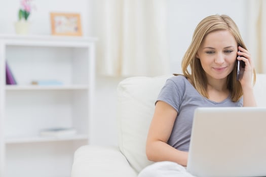 Casual young woman using laptop and cellphone on sofa at home