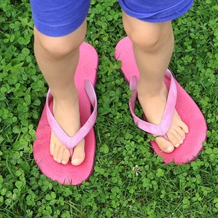 Photograph of small child's feet standing in adult flip flops to symbolize standing in someone else's shoes