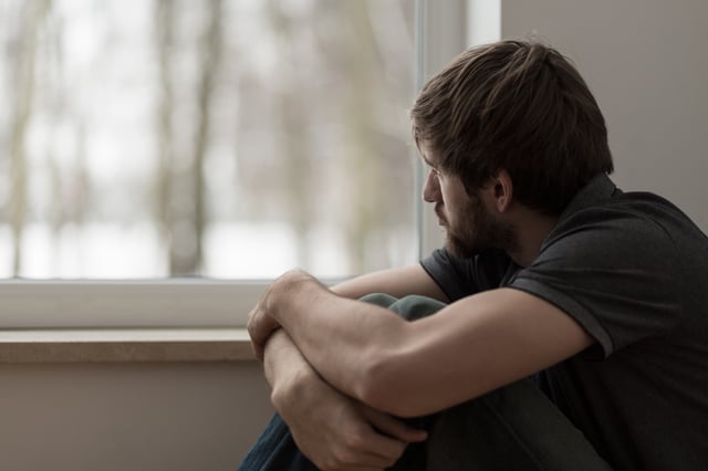 Young man with depression looking out a window