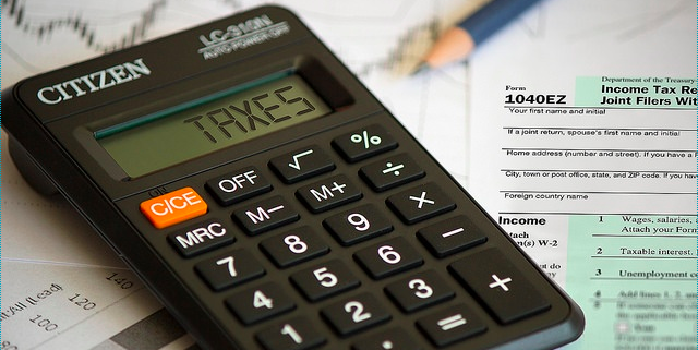A calculator and pen rest on a 1040EZ paper tax form. 