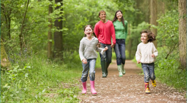 A man, woman, and two children stroll on a path in the woods. 