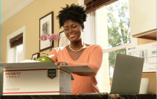 Woman packing into a USPS priority mail box on her home countertop