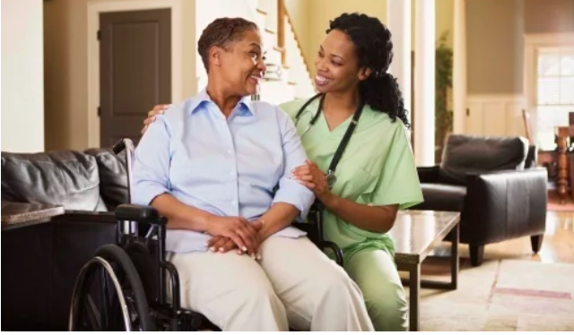 Nurse and woman in a wheelchair smile at each other in living room area during home visit