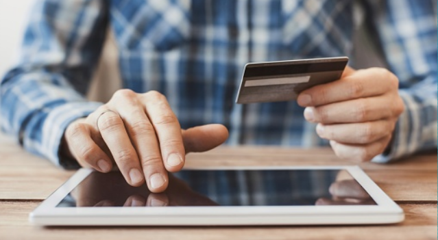 man typing on tablet holding credit card