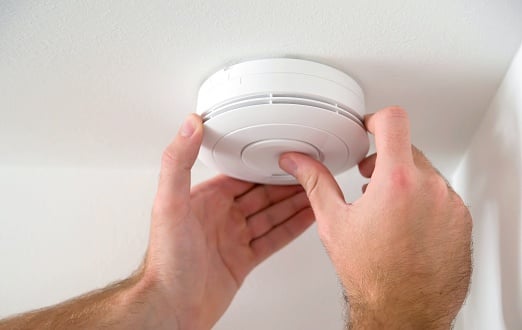 Hand adjusting smoke detector on ceiling