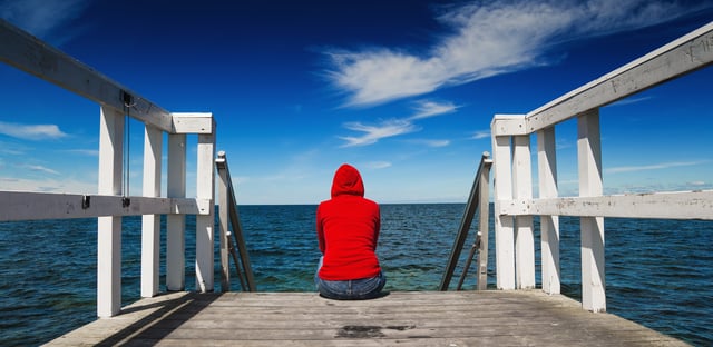 Person sitting looking out on the water at the end of a dock. 