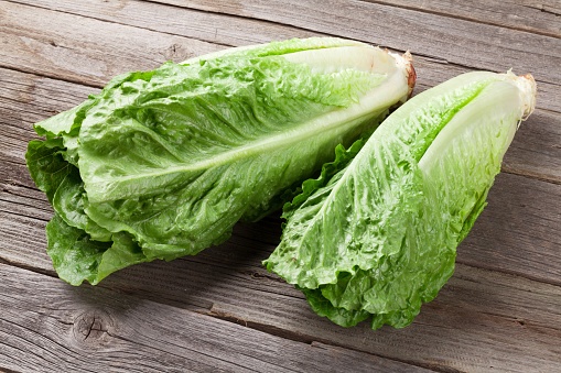 Two heads of romaine lettuce on a wooden table. 