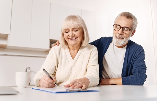 Older couple signing document together on kitchen counter