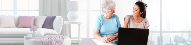 A young home health aide helps an older lady fill out paperwork