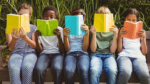 A row of children read books. Link goes PBS' page on summer learning.