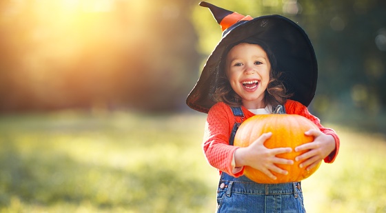 Young girl in a witch's hat smiling and holding a pumpkin