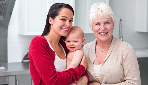 A young, smiling woman holds a baby beside an older smiling woman.