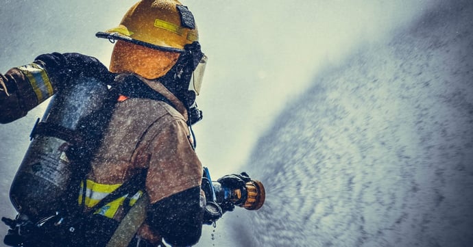 Fireman wearing protective equipment, holding a water hose spraying water