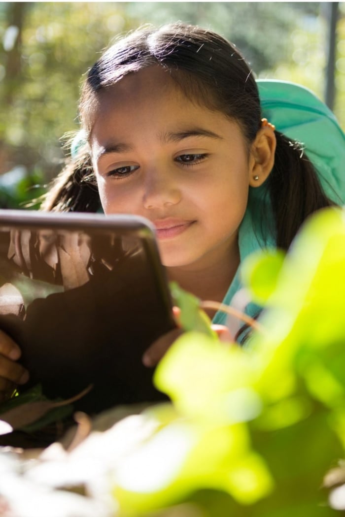 little-girl-with-backpack-lying-on-ground-using-her-tablet-on-a-sunny-picture-id892944456
