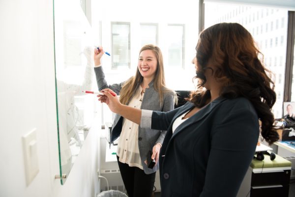 Two women writing on a whiteboard