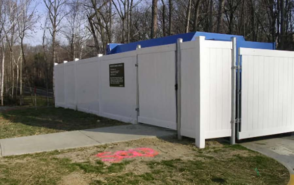 This white commercial Vinyl dumpster enclosure  fits around a local trash company's blue oversized dumpster.