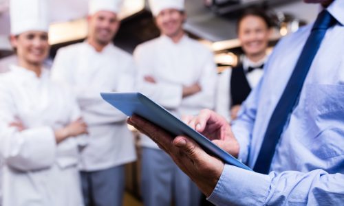 Businessman checking food safety using a tablet in front of four chefs