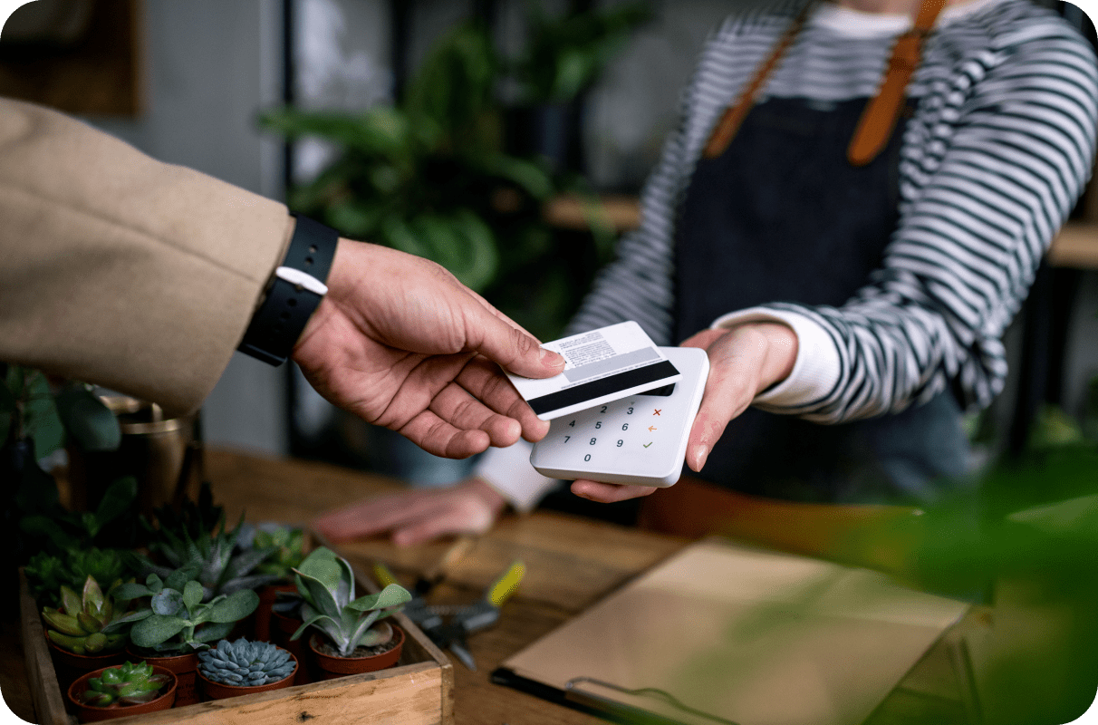 A cashier at a plant shop accepts a tapless credit card payment from a customer