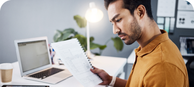 A man in a brown shirt sits at his desk reading a piece of paper