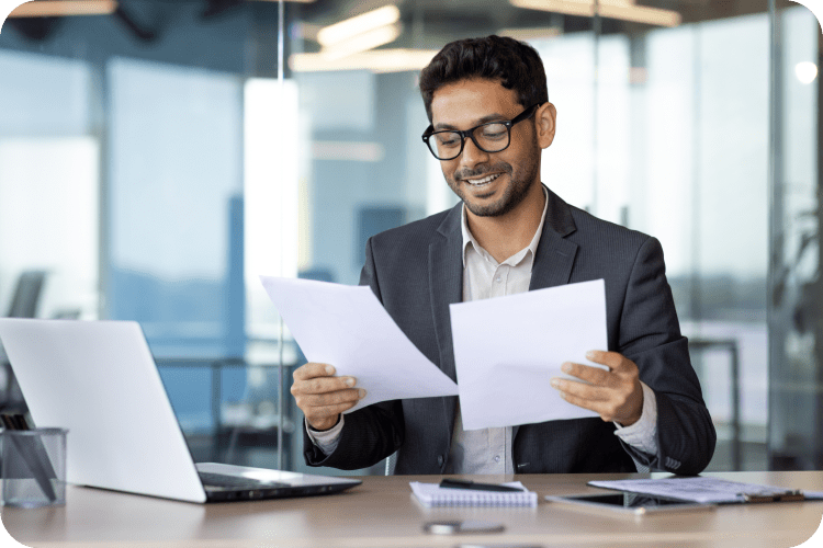 A man in a gray blazer and glasses reviews financial reports