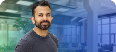 A man in a grey shirt smiling in his office