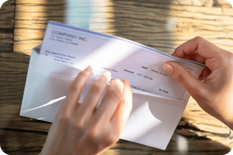 A pair of hands opens up a computer-printed check from an envelope