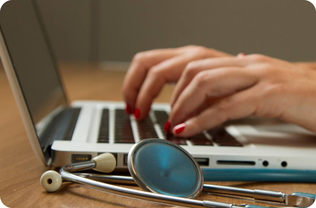 A pair of hands typing on a laptop next to a stethoscope