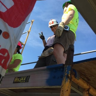 CJ CJ Fitzsimmons giving a peace sign next to some volunteers on a construction platform.