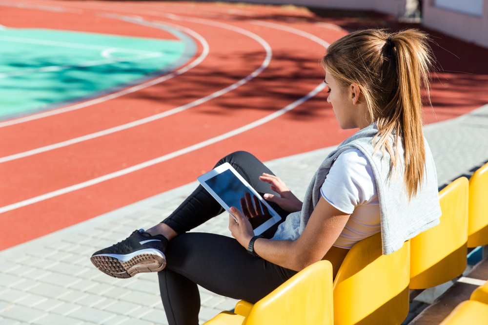 Portrait of a fitness woman resting with tablet computer at outdoor stadium.jpeg