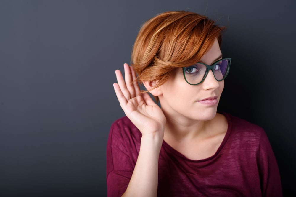 Young woman with a hearing disorder or hearing loss cupping her hand behind her ear with her head turned aside to try and amplify and channel the available sound to her ear drum