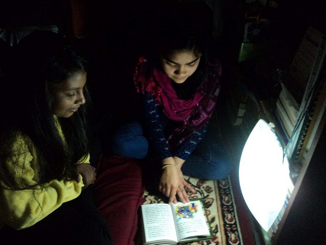 Girls reading book in the dark using light.