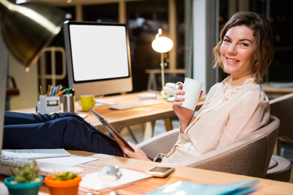 Portrait of businesswoman holding digital tablet and coffee cup at her desk in the office.jpeg