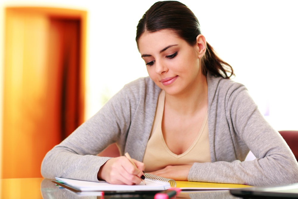 Young beautiful smiling woman writing notes at home.jpeg